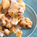 square image of one serving of Crock Pot Apple Cinnamon Roll Casserole with icing on a blue plate