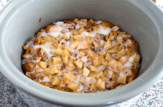 cookedCrock Pot Apple Cinnamon Roll Casserole with icing in a grey slow cooker
