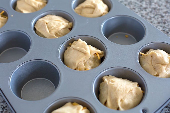 uncooked bacon egg and cheese stuffed crescent rolls in a muffin tin
