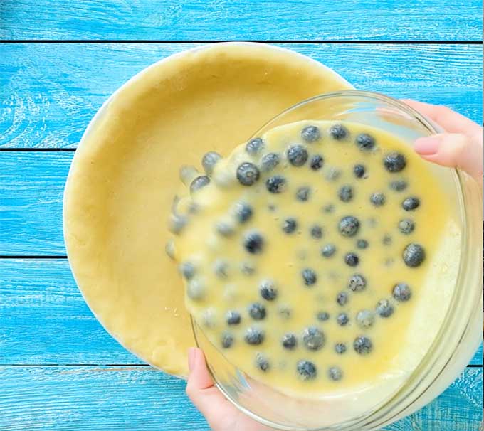 pouring the ingredients for blueberry custard pie into a pie crust
