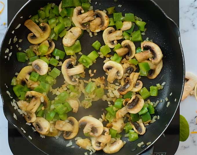 mushrooms, bell peppers, and onions being sautéed in a skillet