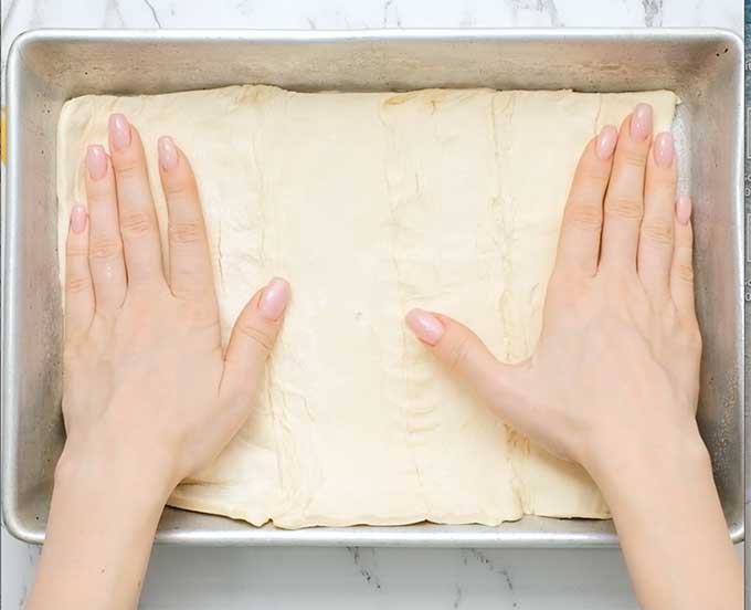 pressing uncooked crescent roll dough into a baking dish