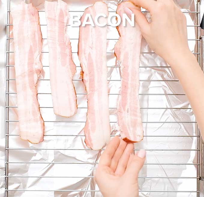 Uncooked strips of bacon being laid on a wire rack over a baking sheet.