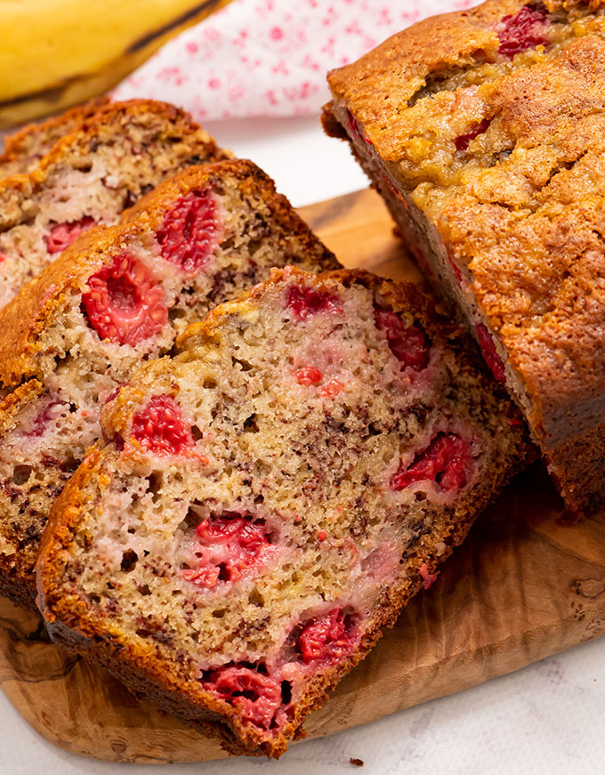 sliced banana bread with raspberries on a cutting board