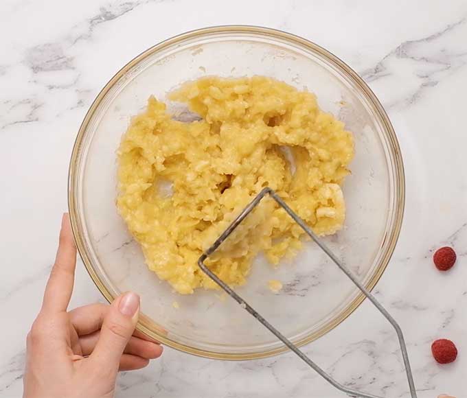 bananas being mashed in a bowl with a potato masher