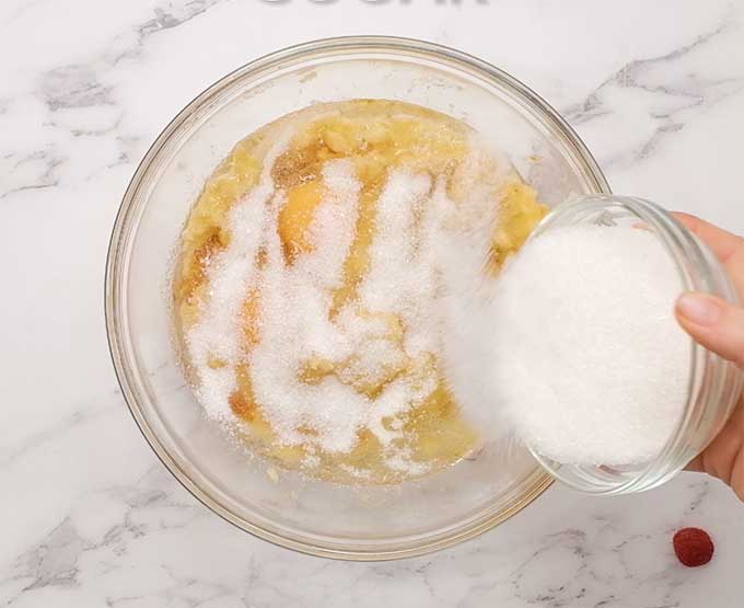 sugar being added to a bowl of mashed bananas