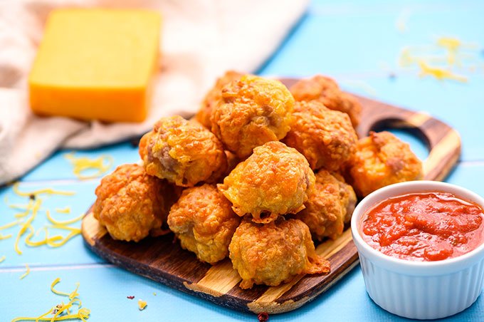 Pile of sausage balls on a cutting board with a side of marinara sauce in a ramekin.