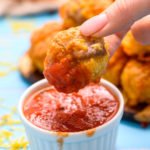 Sausage ball being dipped in marinara sauce in a white ramekin.