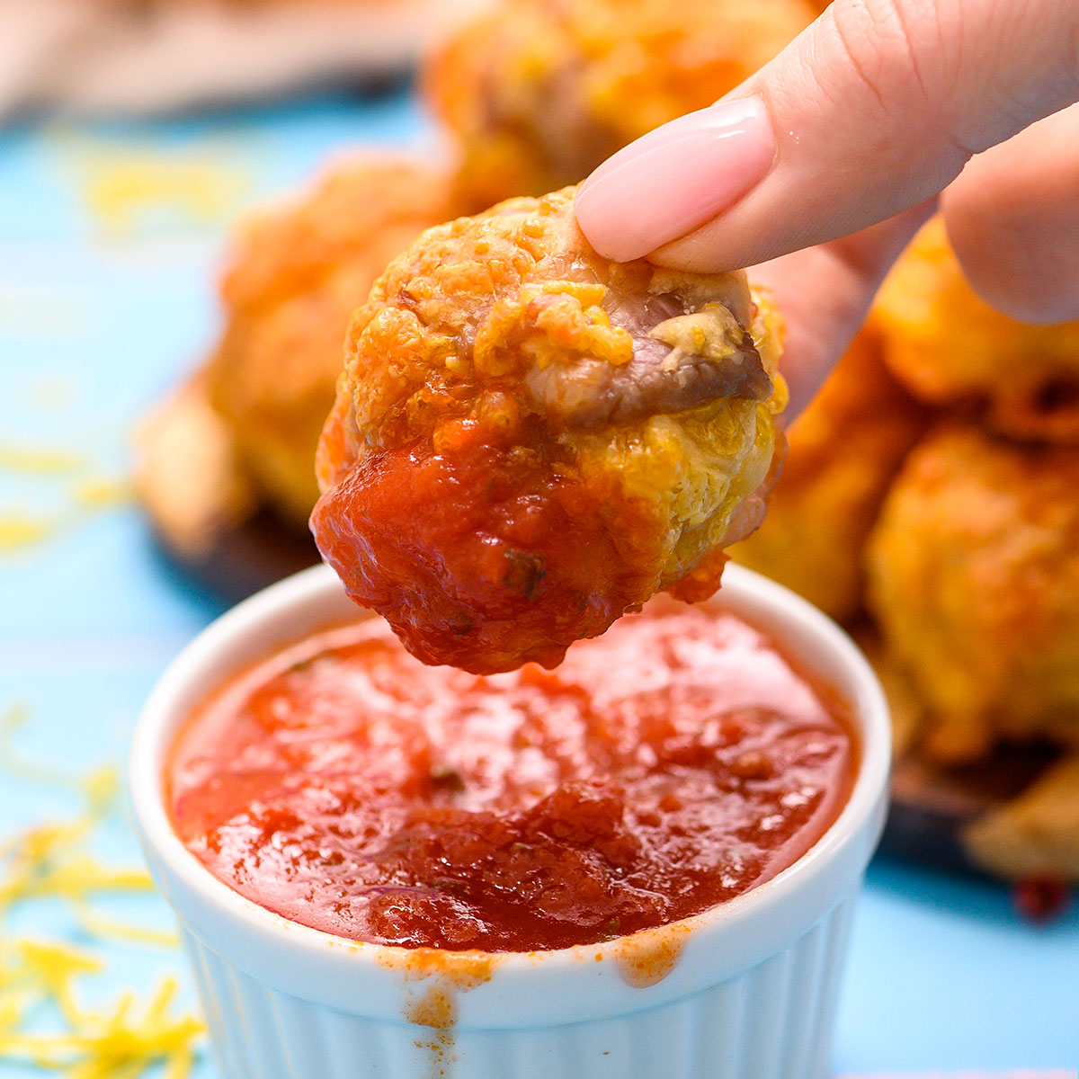 Sausage ball being dipped in marinara sauce in a white ramekin.