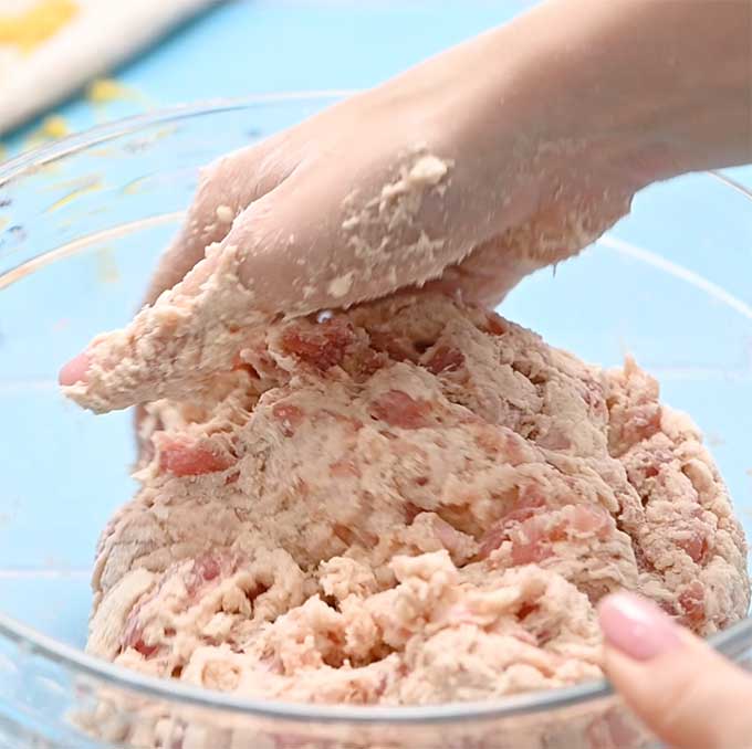 Bowl full of breakfast sausage being mixed by hand with Bisquick baking mix.