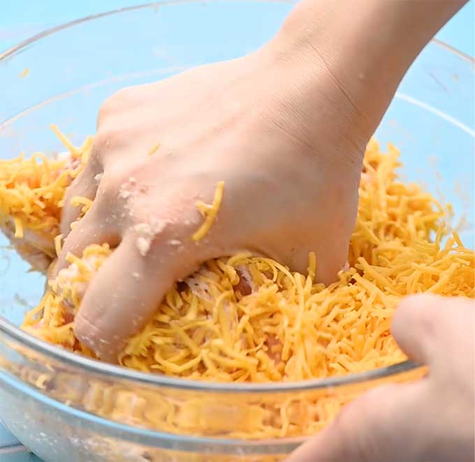 Bowl of sausage, Bisquick, and shredded cheese being hand mixed.