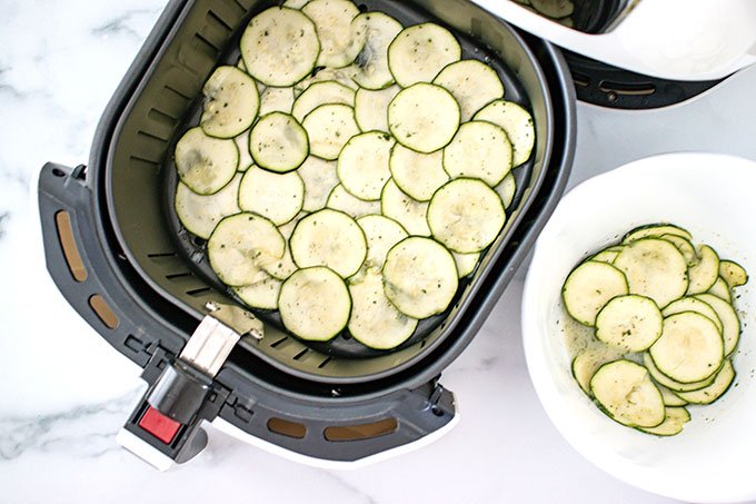Air fryer basket full of thinly sliced zucchini