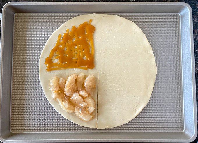 Pie crust with apple pie filling and caramel sauce on half of it.