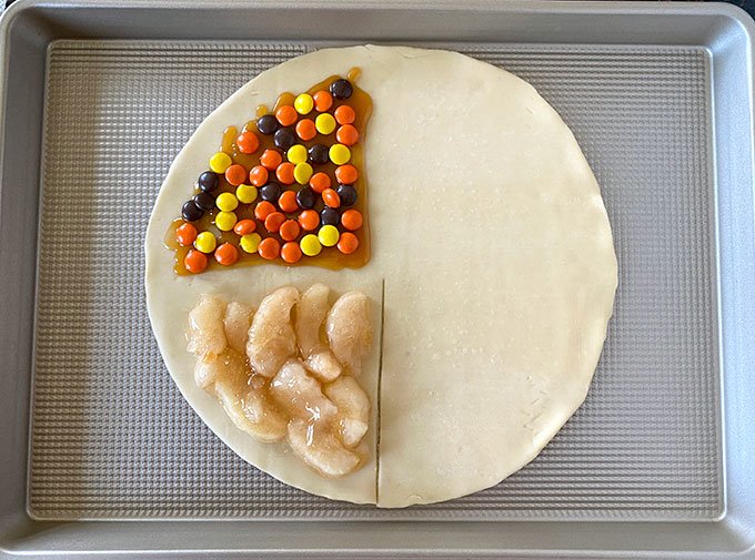 pie crust with apple pie filling, caramel, and reeses pieces on half of it.