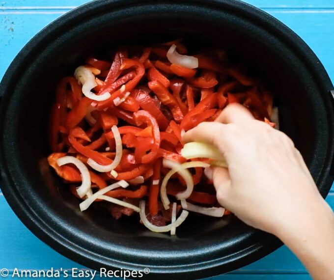 crock pot with peppers and onions being added
