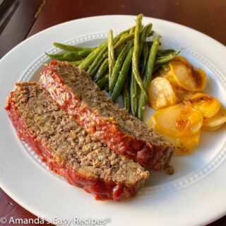 2 sliced of ketchup glazed meatloaf on a plate with 2 sides.