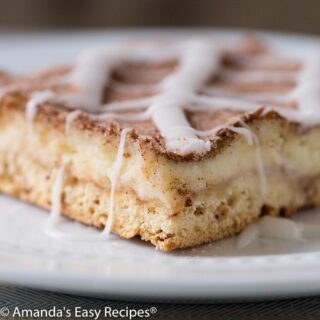 Slice of cinnamon roll cheesecake on a white plate.
