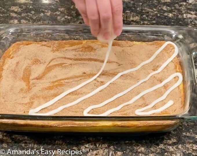 Drizzling the cinnamon roll icing over the cheesecake.