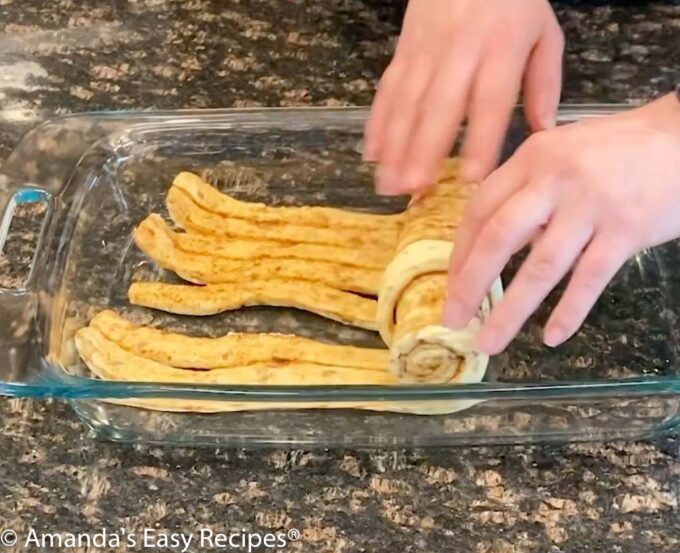 Unrolling cinnamon rolls in a baking dish.