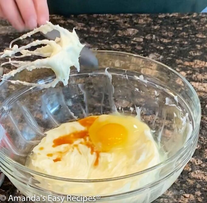 Adding egg and vanilla to cream cheese in a bowl.