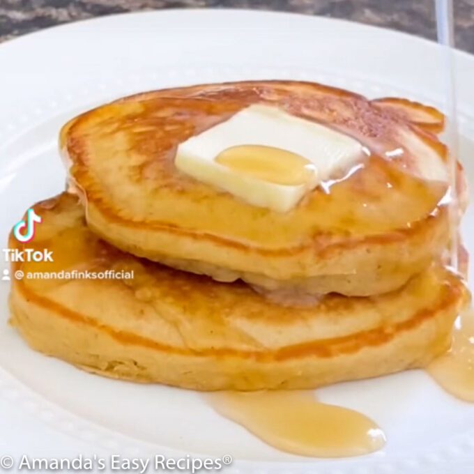 Two brown sugar pancakes on a white plate topped with butter and syrup.