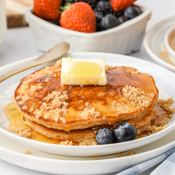 Two pancakes on a white plate topped with butter and syrup.