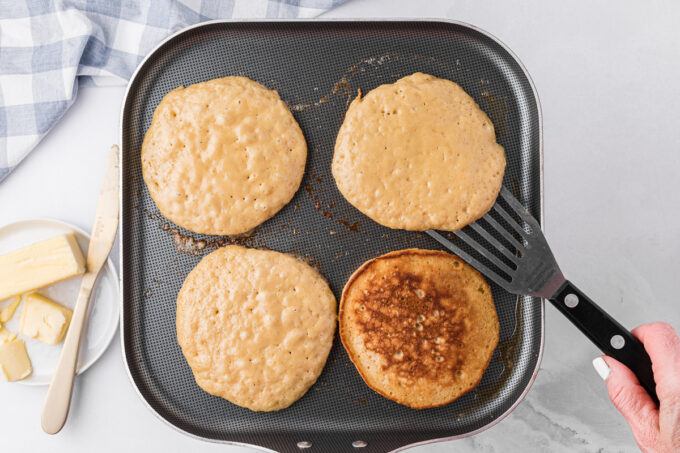 Four pancakes being cooked on a griddle.