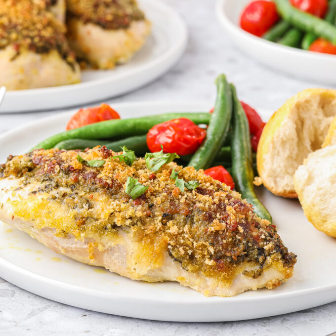 Parmesan pesto baked chicken on a plate with vegetables.