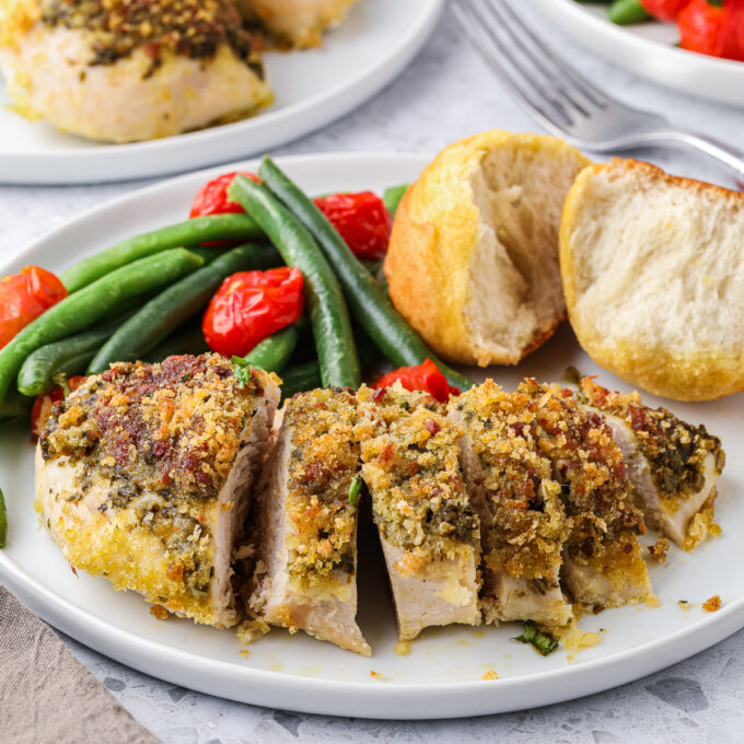 Sliced parmesan pesto baked chicken breast on a plate with vegetables.