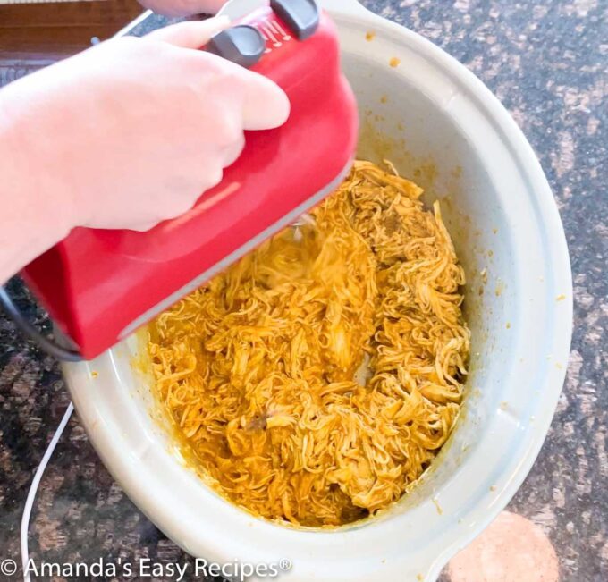 Using a hand mixer to shred chicken in a crock pot.