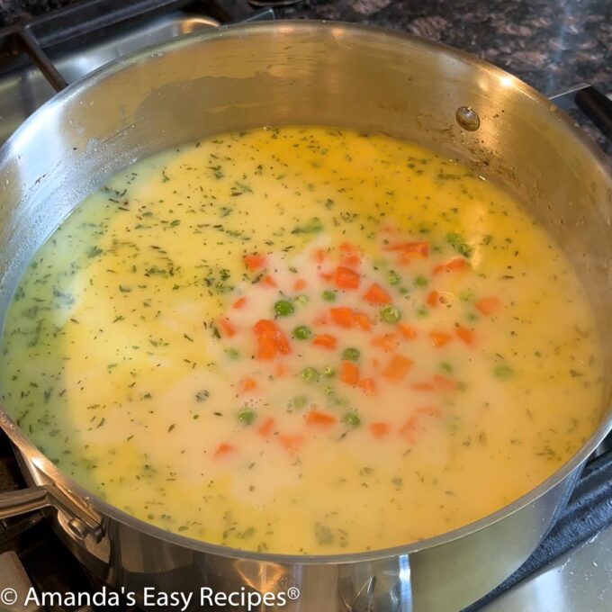 Adding broth, milk, peas and carrots to the pot.