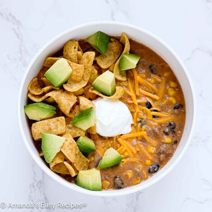 Bowl full of cheesy taco soup topped with cheese, chips, sour cream, and chopped avocado.