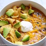 Bowl full of easy cheesy taco soup topped with shredded cheddar, sour cream, chops, and chopped avocado.